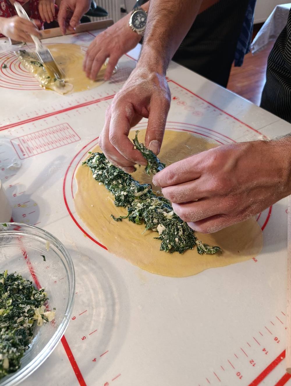 Hands spreading spinach and feta filling onto fresh phyllo dough